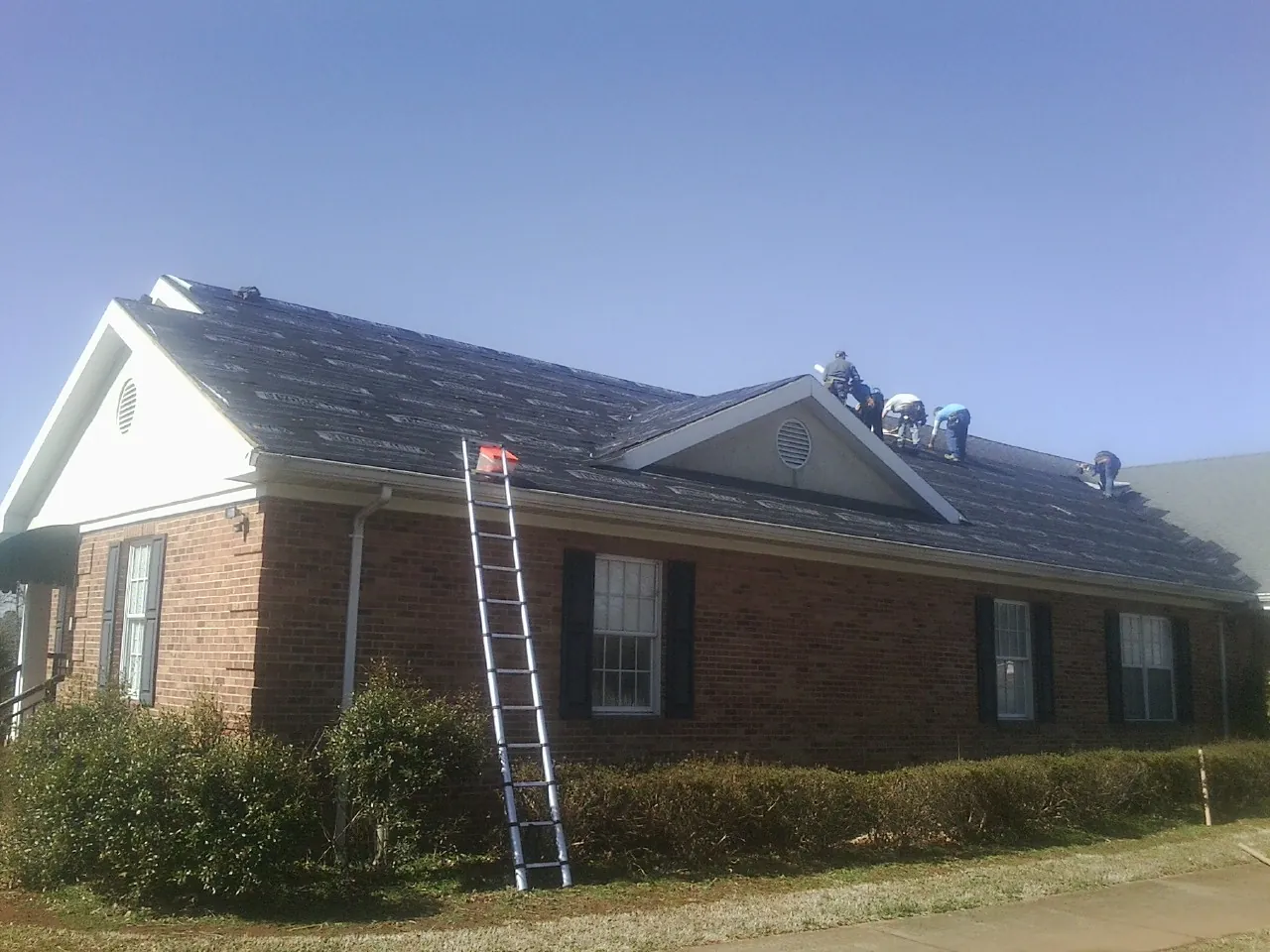 Crew tearing shingles off a brick ranch roof with a ladder set — Emergency Roof Repair work by our crew in Bantam