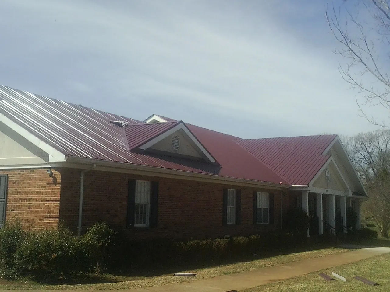 Red metal roof with gabled entries on a long brick building, from a Hail Damage Roof Repair job in Bantam