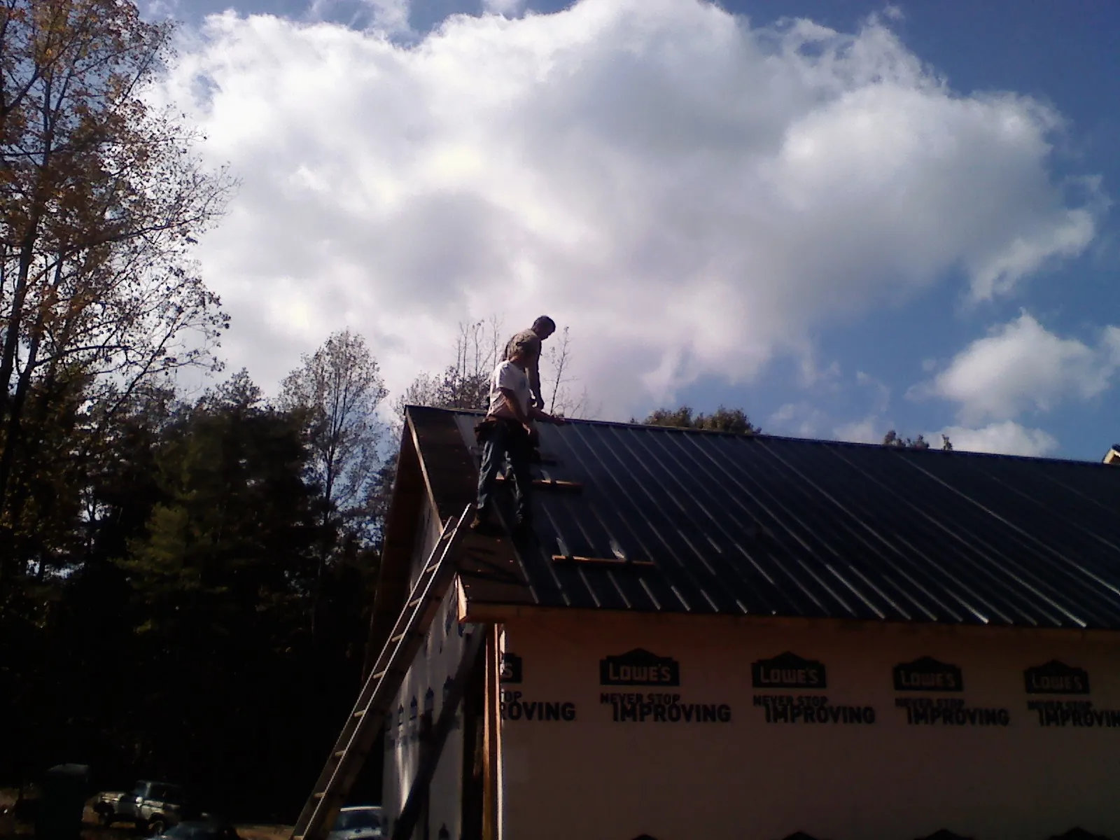 Roofer fastening dark metal panels high against a cloudy sky, from a Roof Inspection job in Bantam