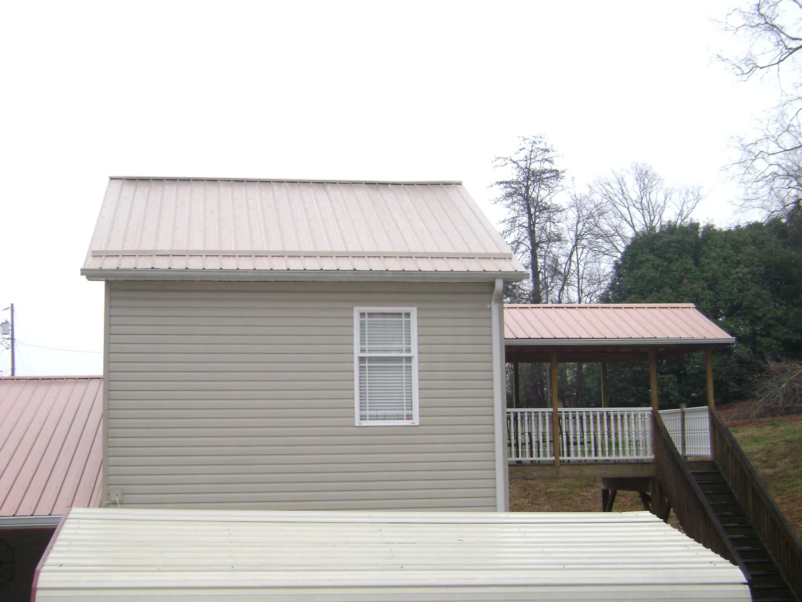 Tan metal roofs on a two story addition and attached porch, from a Roof Replacement job in Bantam